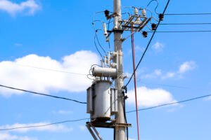 High Electric voltage wires and pole power lines,electric towers,power transformer against vibrant blue sky, clouds and sun